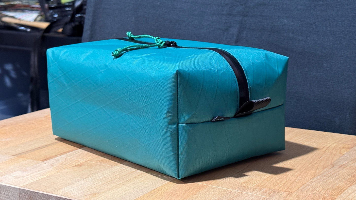 Teal bag with a black strap on a wooden surface with a blue curtain in the background